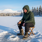 Man i svarta vinterbyxor sitter på en pall och isfiskar på en frusen fjällsjö i sol