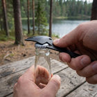 Multiskedens flasköppnare hakad under kapsylen på en glasflaska vid ett campingbord i skogen