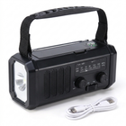 Svart beredskapsradio med ficklampa i kortsidan, bärrem, FM/AM-skala och vit USB-C-kabel på vit bakgrund