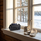 Beredskapsradio med solcellen uppåt på ett fönsterbräde i en stuga, snötäckt skog och sjö utanför