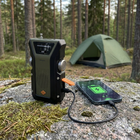 Vevradion laddar en mobil via USB-kabel på en sten vid tältet, mobilskärmen visar en laddningssymbol