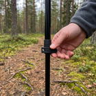 Tumme stänger snabblåset på en vandringsstav, skogsstig i bakgrunden