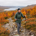 Kvinna vandrar med stavar på en stenig fjällstig bland höstfärgad björk